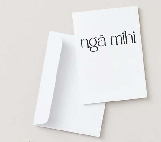 Te Reo Māori card flat lay. The card is white with the words "ngā mihi" on the front in black font. The card is sitting on top of a white envelope. 